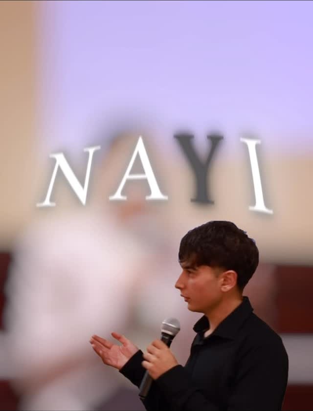 NAYI founder Alexander Kasumyan speaking at a NAYI event, with NAYI in serif type projected behind him.